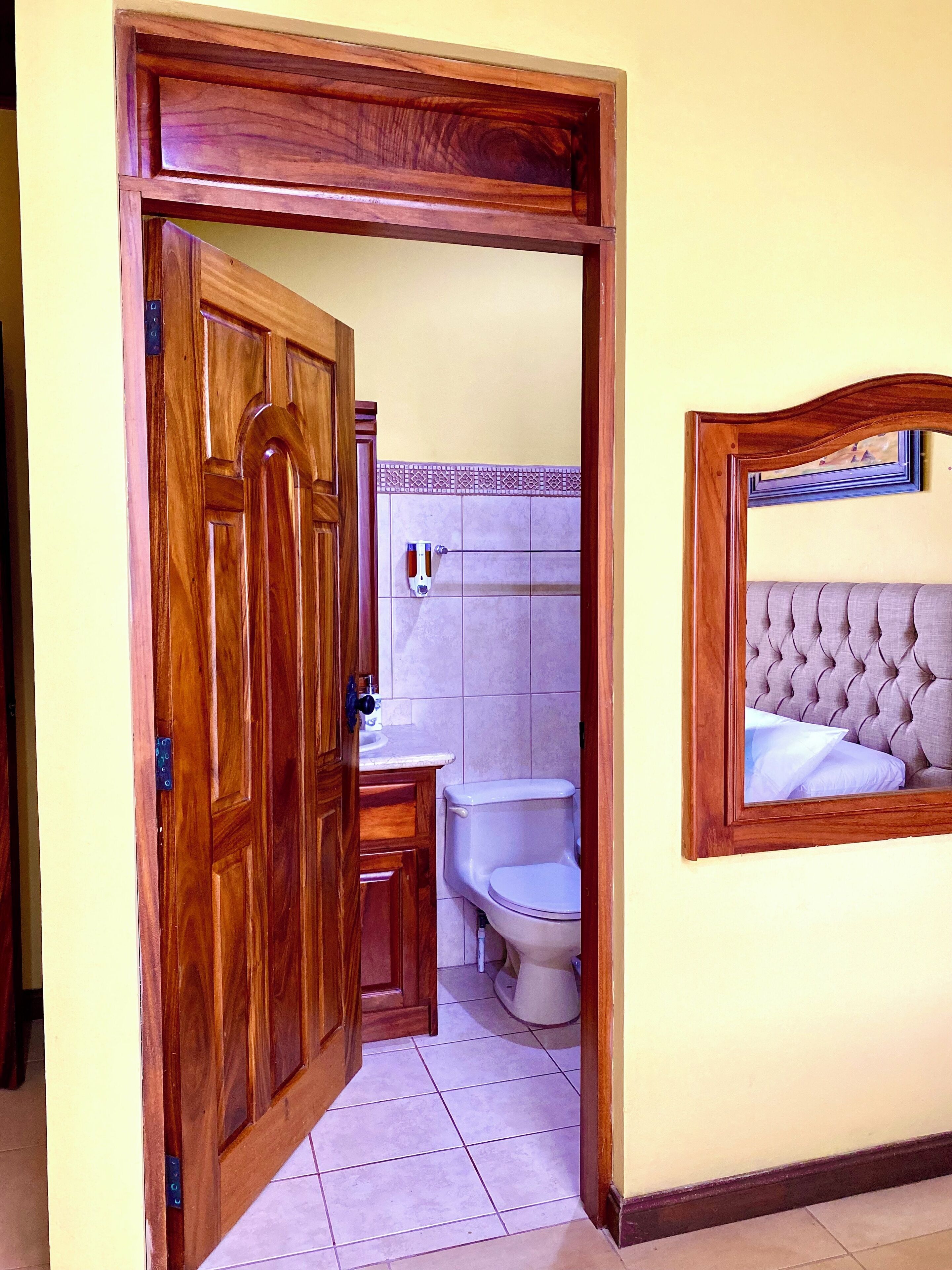 A wooden door leading to a bathroom with a toilet, sink, and tiled walls.