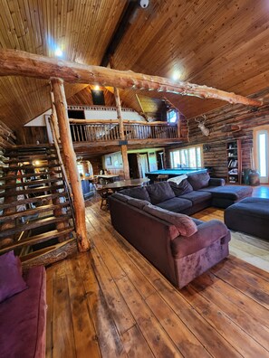 A rustic cabin interior with a wooden staircase, a pool table, a sofa, and a dining area. - Larsen Rustic Secluded Log Cabin W/Outdoor Hot Tub (Wauzeka)