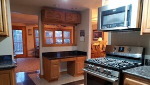 Une cuisine avec des meubles en bois, une cuisinière à gaz, un four à micro-ondes et une grande fenêtre.