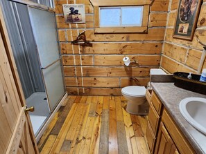 A wooden cabin bathroom with a toilet, sink, and shower.