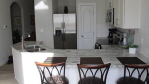 Uma cozinha moderna com ilha central, eletrodomésticos de aço inoxidável e micro-ondas sobre a bancada.