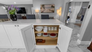 A modern kitchen with a built-in pantry, marble flooring, and a dining area with a TV and artwork.