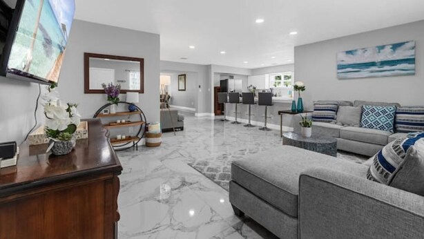 A modern living room with a marble floor, grey sofa, and a flat-screen TV mounted on the wall.