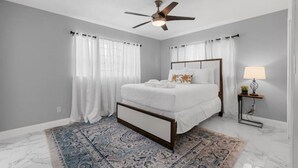 A bedroom with a bed, a ceiling fan, a nightstand with a lamp, and a patterned rug.