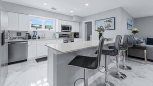 A modern kitchen with white cabinets, a central island with bar stools, a microwave, and a dishwasher.