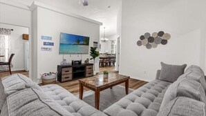Ein geräumiges Wohnzimmer mit einem grauen Ecksofa, einem Holztisch und einem an der Wand montierten Fernseher.