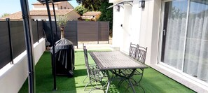 Eine Terrasse mit Tisch und Stühlen, einem überdachten Grill und einer Schiebetür.