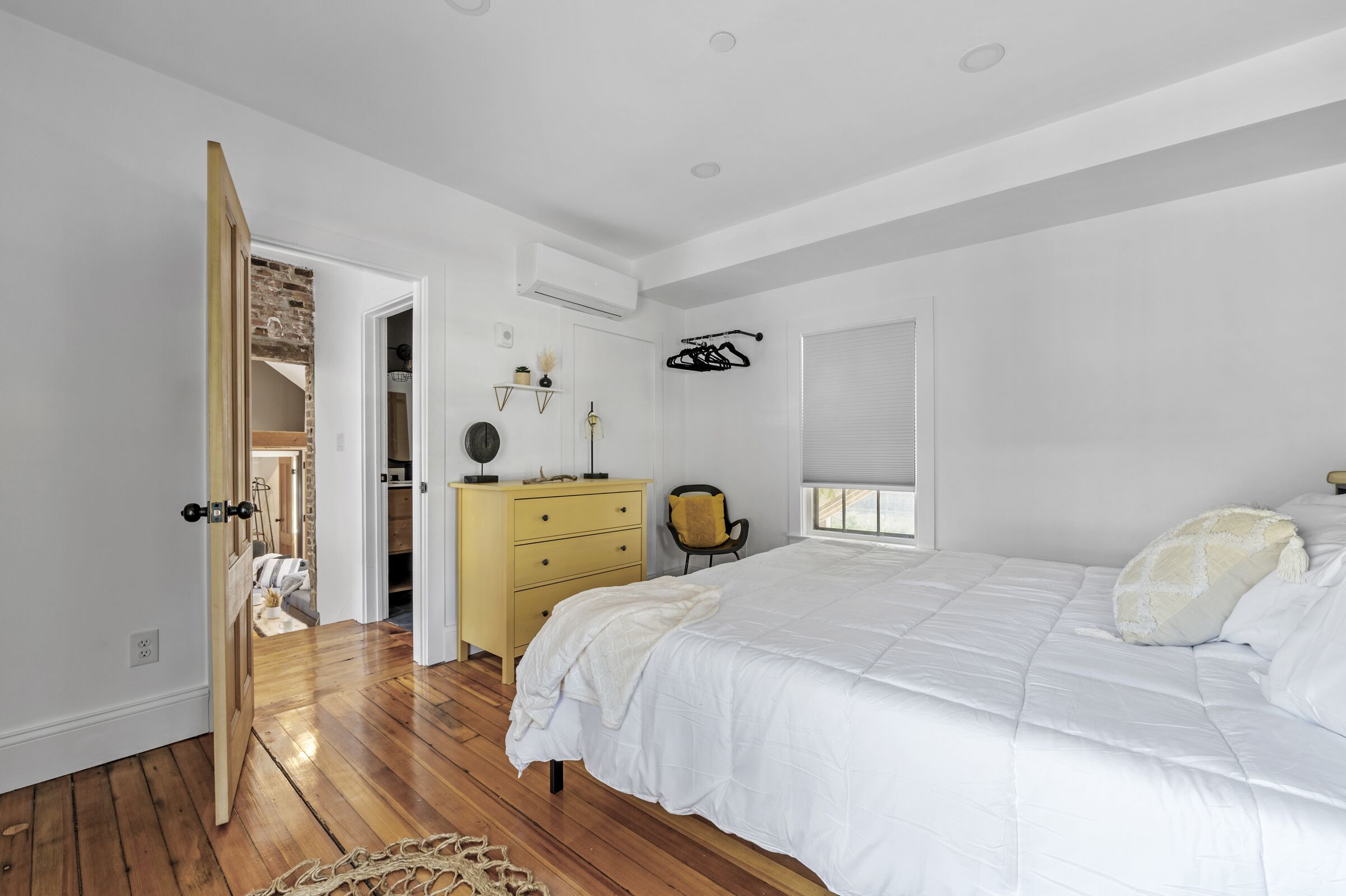 A bedroom with a large bed, wooden flooring, a dresser, and a closet with a brick wall.