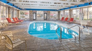 Une piscine intérieure dotée d’un sol en pierre, de chaises longues rouges et de grandes fenêtres.