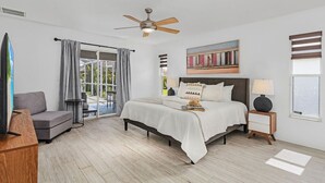A bedroom with a bed, a ceiling fan, a TV, a sofa, a nightstand, and a window with blinds. - The Coral Reef Oasis (Cape Coral)
