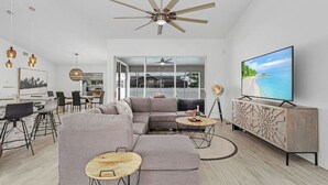 A modern living room with a large sectional sofa, a TV, and a ceiling fan. - The Coral Reef Oasis (Cape Coral)