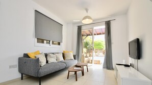 Un salon moderne avec un canapé gris, une petite table en bois, un téléviseur à écran plat et une porte-fenêtre coulissante donnant sur un espace extérieur.