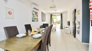 Un coin repas avec une table en bois dressée pour quatre personnes, des chaises, une bouteille de jus d’orange et une assiette de fruits.