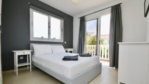Une chambre à coucher comprenant un lit, une table de chevet, une commode et un balcon avec des rideaux.