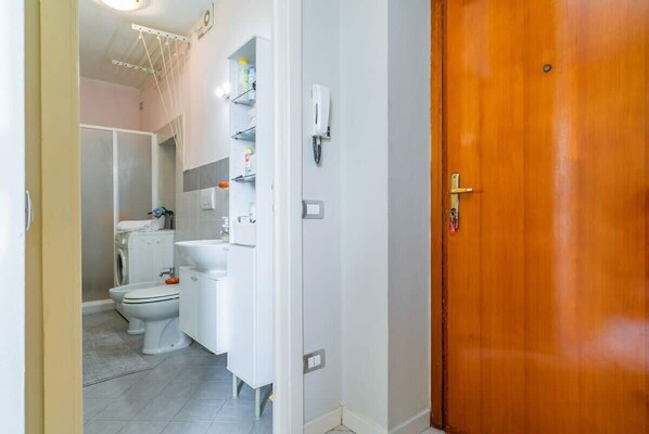 A bathroom with a toilet, sink, and shelves with toiletries.