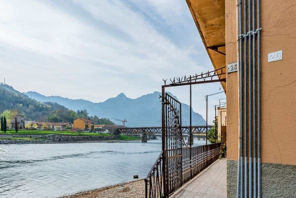 A riverside walkway with a metal gate, a bridge in the background, and mountains.