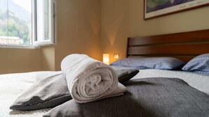 Ein ordentlich gemachtes Bett mit einem zusammengerollten Handtuch, einem Kissen und einem Bild an der Wand.