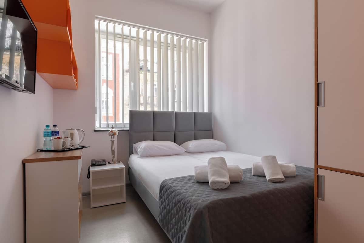 A hotel room with a bed, bedside table, and a window with blinds.
