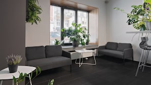 A modern living room with a grey sofa, a white coffee table, and a grey armchair. There are several potted plants on the windowsill and a plant on the floor. - ESPERANTO HOME (Katowice)