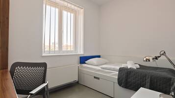 Une chambre à coucher comprenant un lit, un bureau, une chaise et une fenêtre avec des stores.