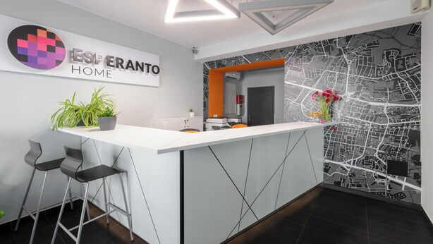 A modern reception area with a white counter, two bar stools, a potted plant, and a wall map. - ESPERANTO HOME (Katowice)