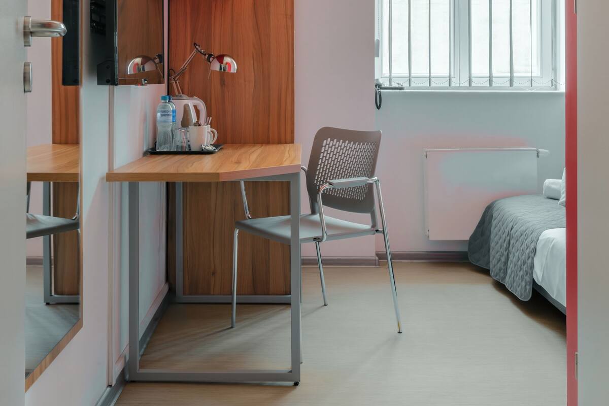 A modern room with a wooden desk, a chair, a bed, a window with blinds, and a radiator.