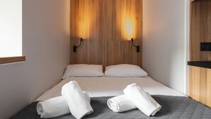 A hotel room with a wooden headboard, two beds with white linens, and two rolled towels on the bed. - ESPERANTO HOME (Katowice)