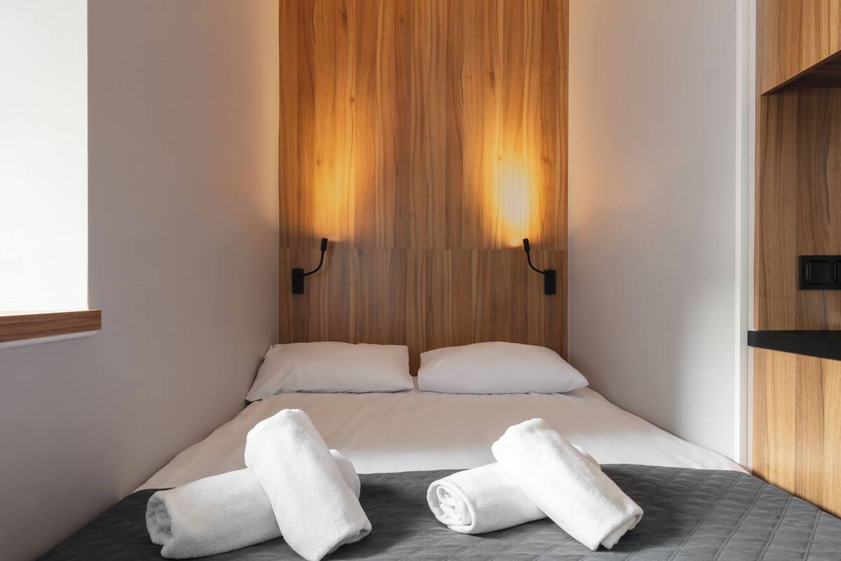 A hotel room with a wooden headboard, two beds with white linens, and two rolled towels on the bed.