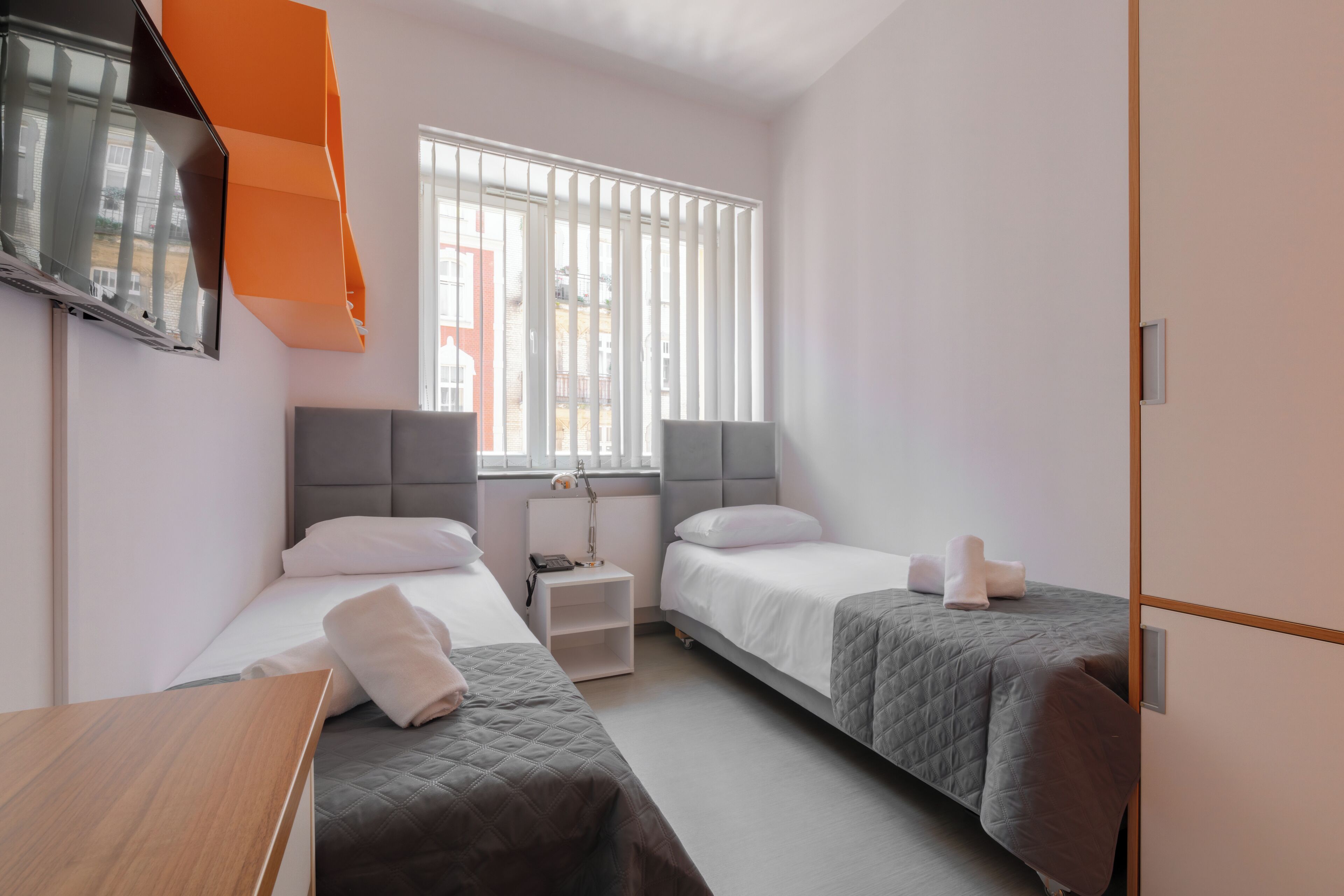 A hotel room with two beds, a TV mounted on the wall, and a window with blinds.