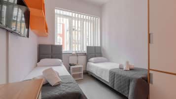 A hotel room with two beds, a TV mounted on the wall, and a window with blinds.