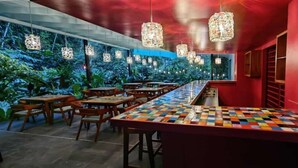 En restaurang med en lång bardisk, träbord, hängande lampor och en röd vägg.