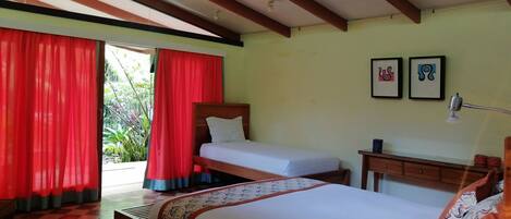 Quarto com cama, escrivaninha e cadeira. Possui duas janelas com cortinas vermelhas.