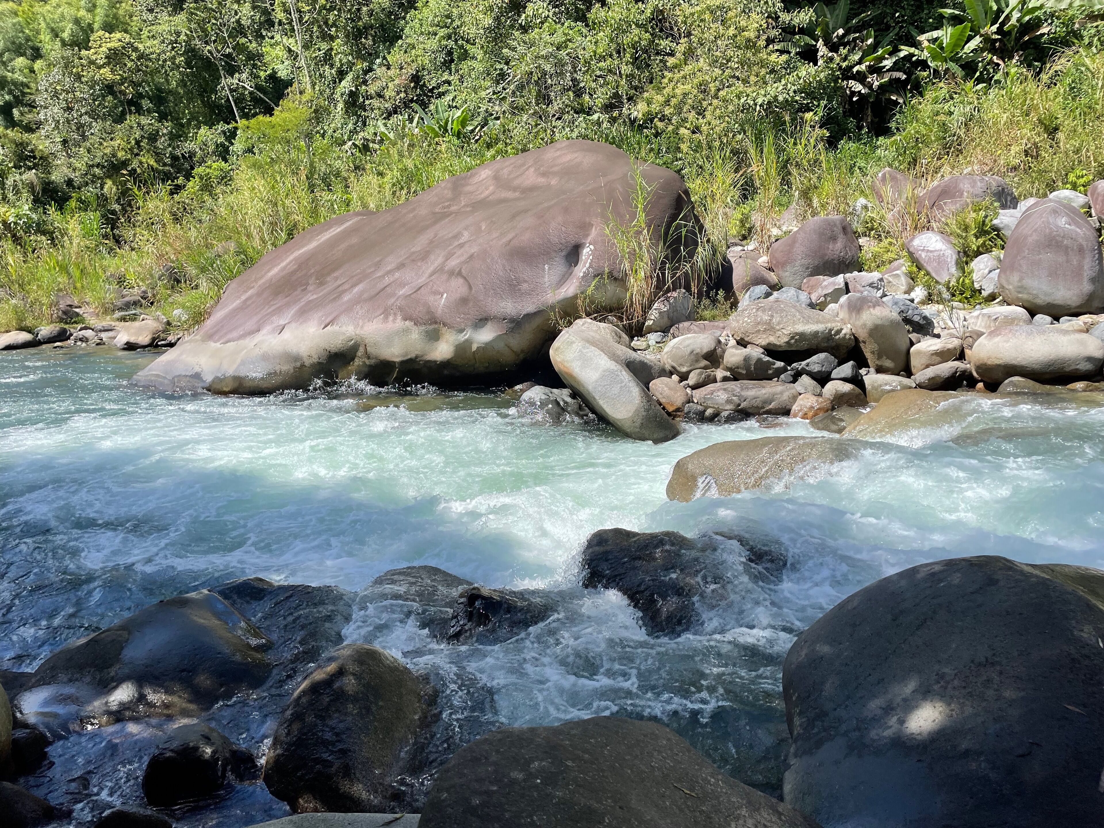 A river flowing through a rocky landscape with large boulders and dense greenery in the background.