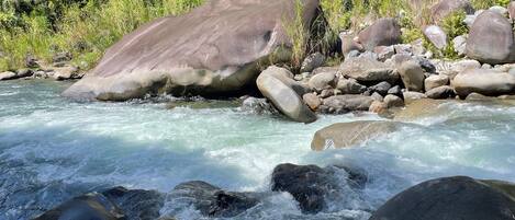 A river flowing through a rocky landscape with large boulders and dense greenery in the background.