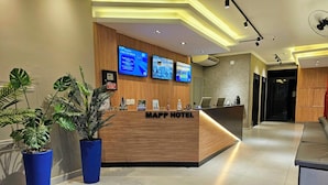A hotel reception area with a wooden reception desk, multiple screens, and potted plants. - MAPP HOTEL (Aparecida)