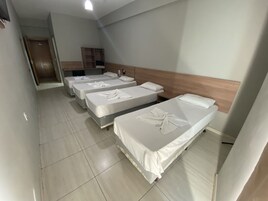 Habitación de hotel con tres camas individuales, cabecero de madera, un escritorio pequeño y un armario.