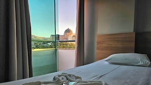 A hotel room with a bed, a window with curtains, and a view of a building with a dome. - MAPP HOTEL (Aparecida)