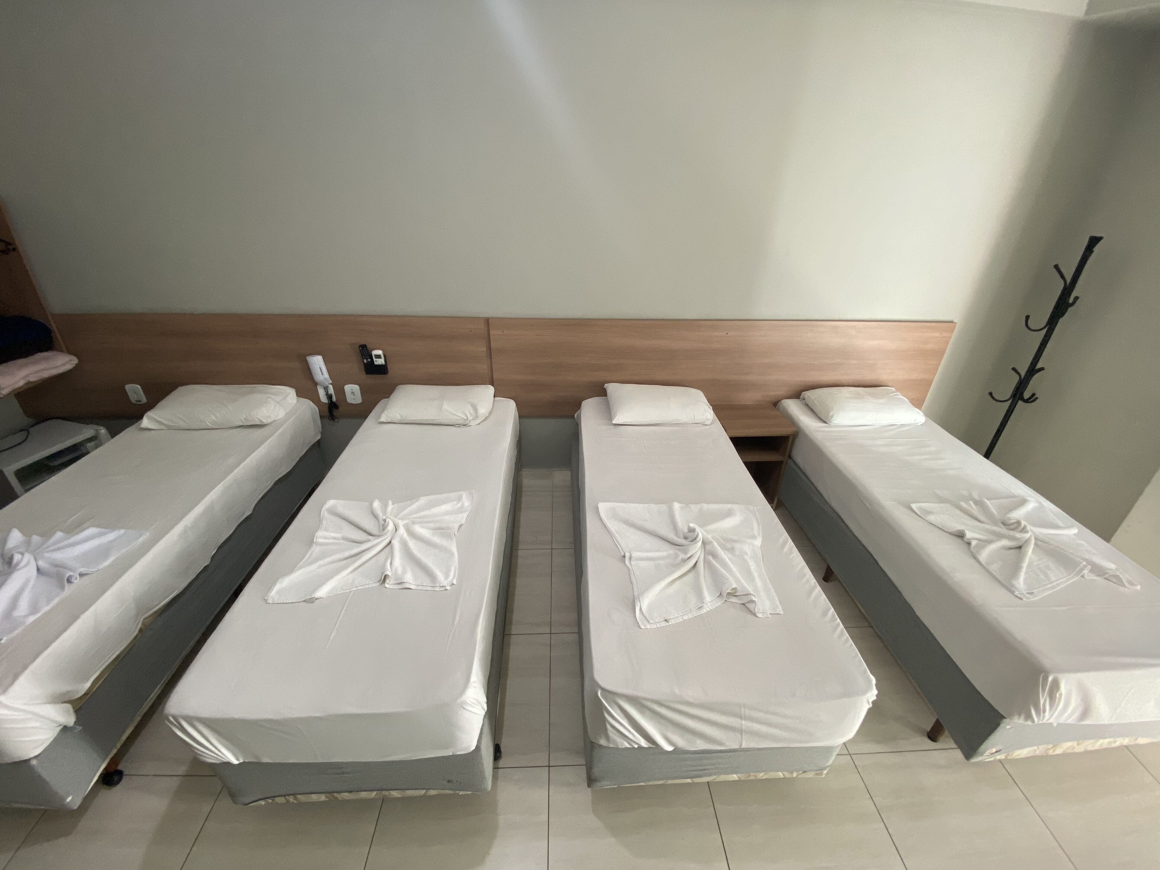 Habitación de hotel con cuatro camas individuales, cada una con una toalla blanca doblada con cuidado.