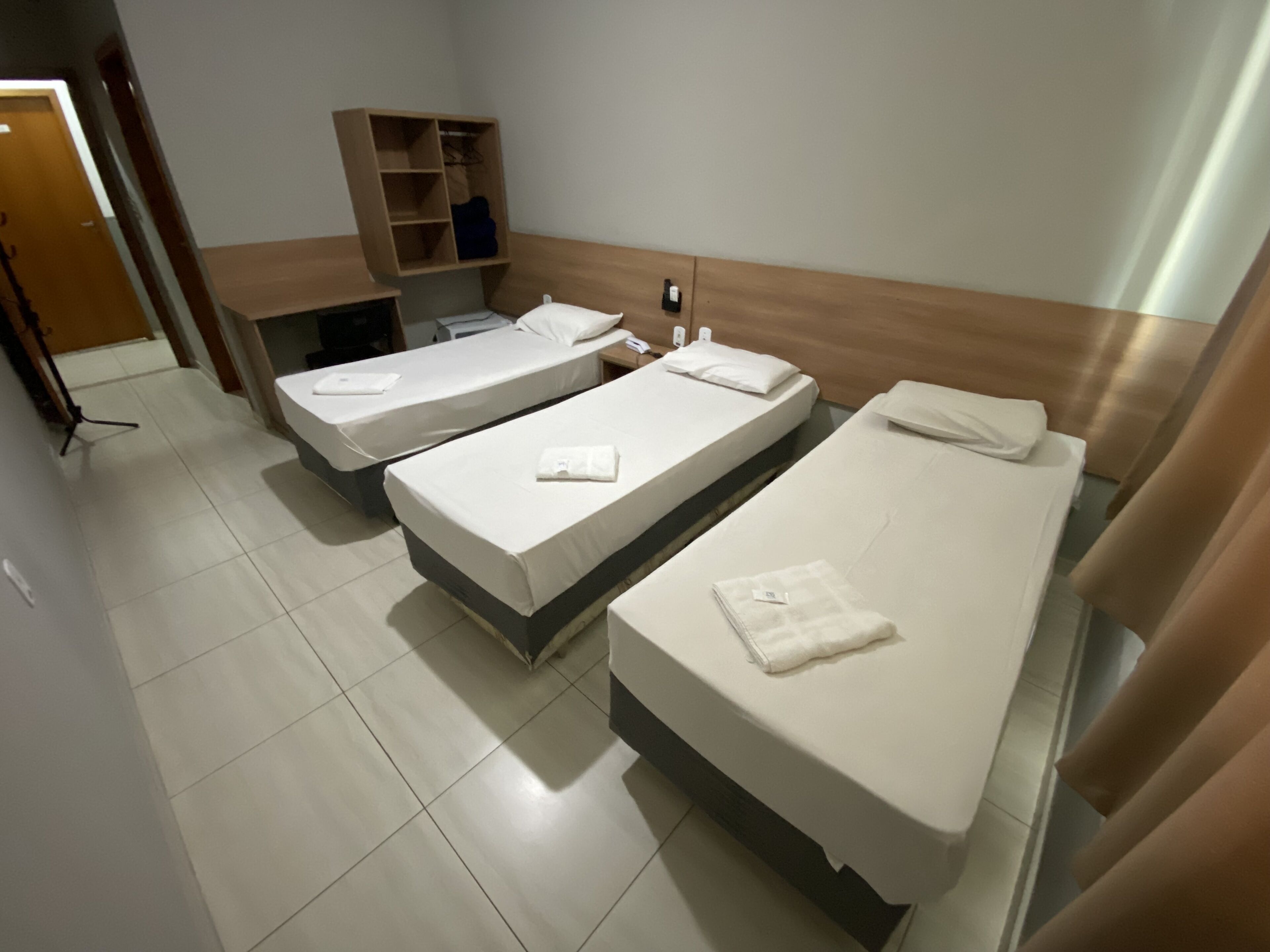 A hotel room with three single beds, a wooden wardrobe, and a small desk with a chair.