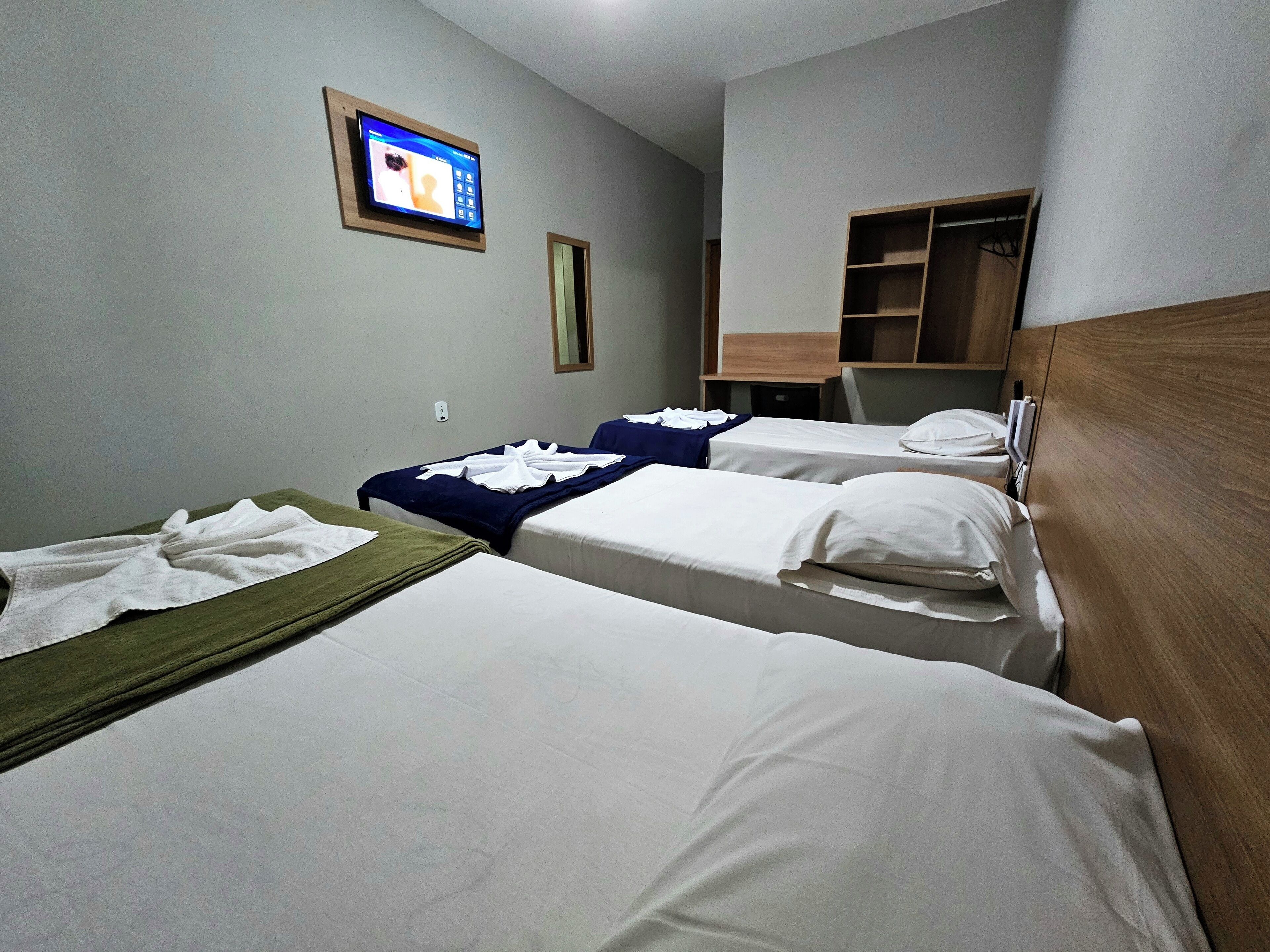 A hotel room with three single beds, a television on the wall, and a wooden wardrobe.