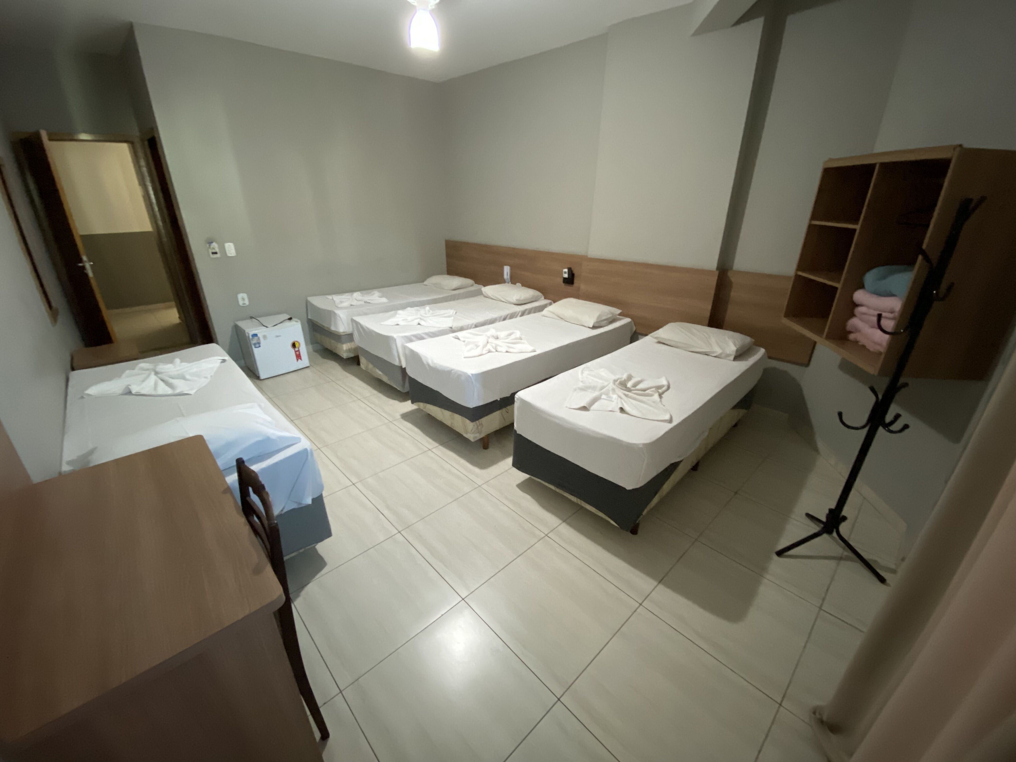 A hotel room with four single beds, a desk, a chair, a wardrobe, and a mirror.