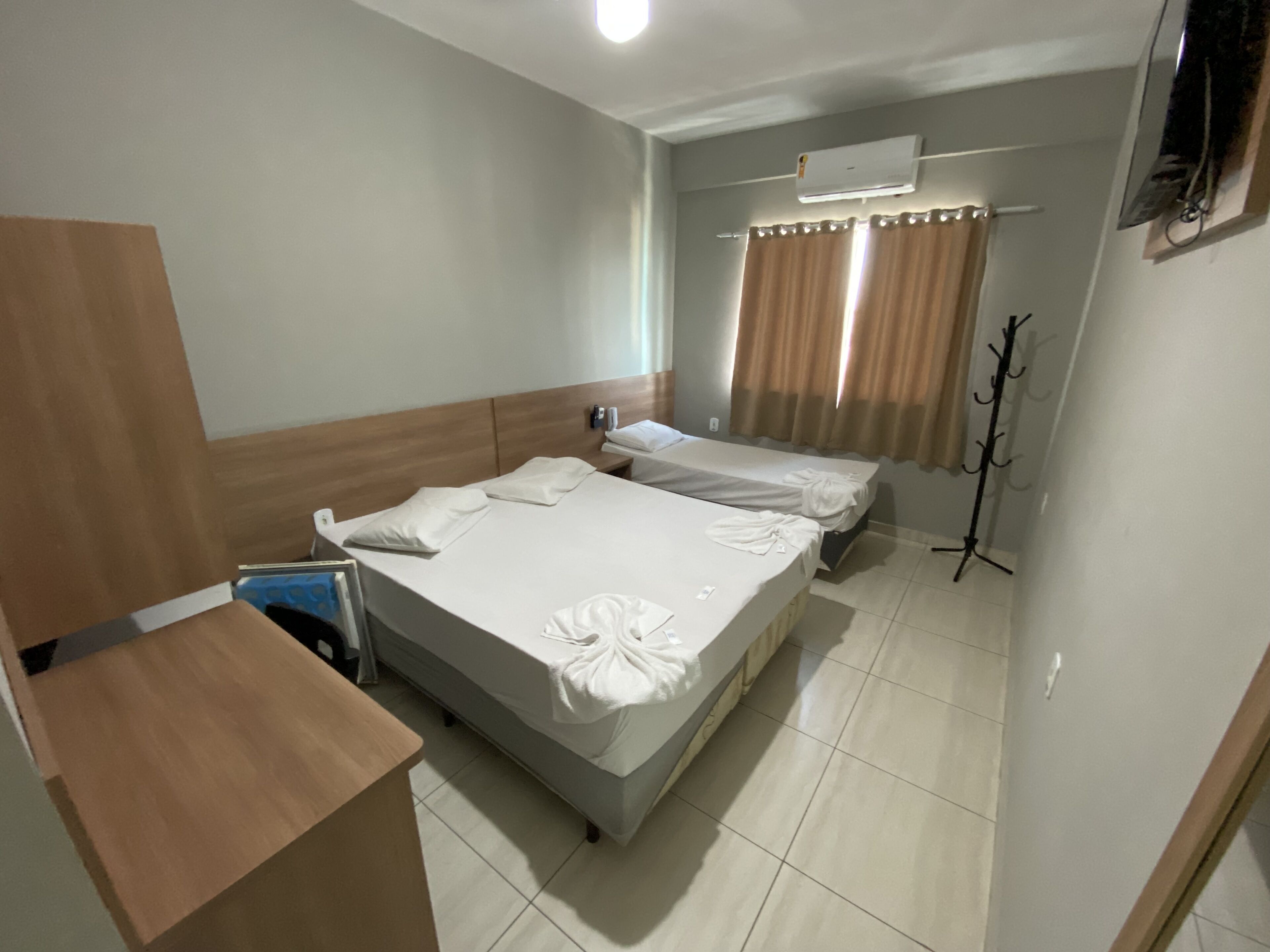 A hotel room with two beds, a wooden desk, a coat rack, and an air conditioning unit.