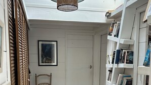 A narrow hallway with a wooden chair, a bookshelf, and a framed picture on the wall. - Maison DE Ville Vallon DES Auffes (Marseille)