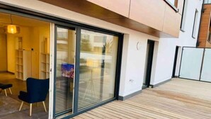 A modern apartment with a wooden deck, a blue chair, and a glass door leading to a room with shelves.