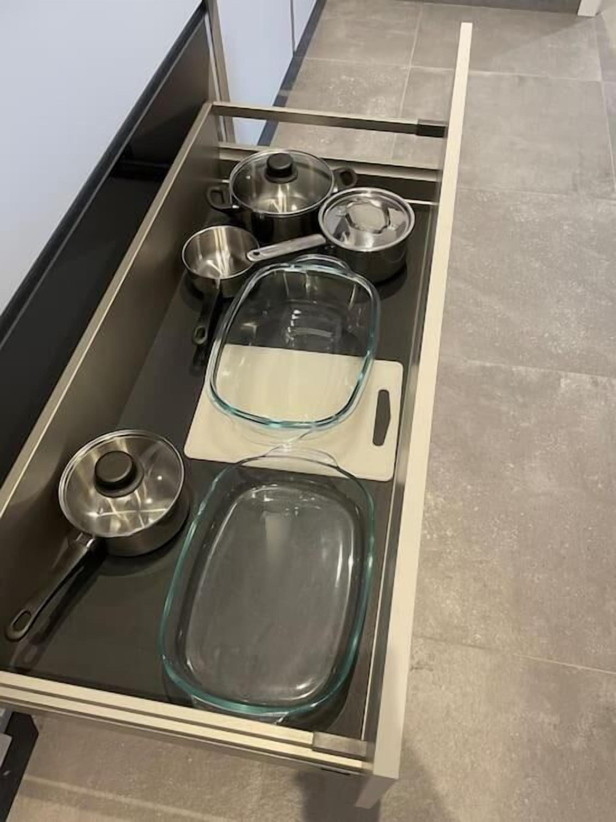 Un tiroir de cuisine contenant divers ustensiles de cuisine, notamment des casseroles, des poêles et un plat de cuisson en verre.