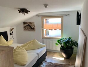 A bedroom with a bed, a wooden headboard, a window with a view of buildings, a plant, and a radiator.