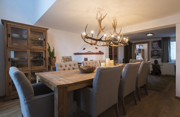 A dining area with a wooden table, upholstered chairs, a chandelier with antlers, and a cabinet with glass doors.