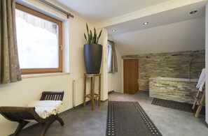 A room with a wooden chair, a large potted plant, a radiator, a stone wall, and a shower area.