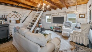 Interior acogedor de una cabaña con techo de madera, un sofá, sillones, un televisor y una escalera.