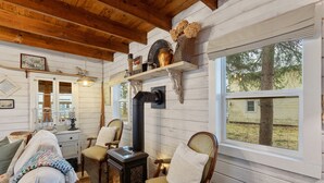 Interior acogedor de una cabaña con estufa de leña, asientos cómodos y ventana con vista a un jardín.